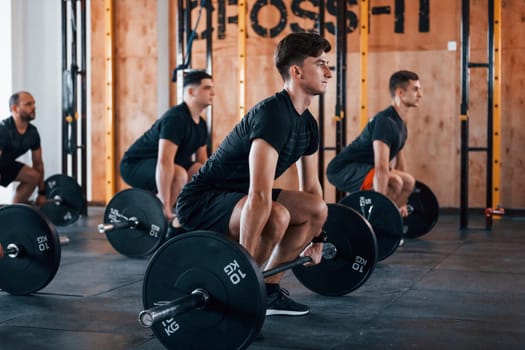 Busy by doing exercises. Group of young sportive people have crossfit day indoors in gym.