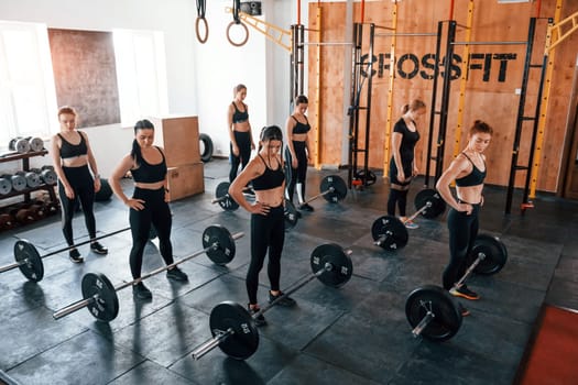 Together with barbells. Group of young sportive people have crossfit day indoors in gym.