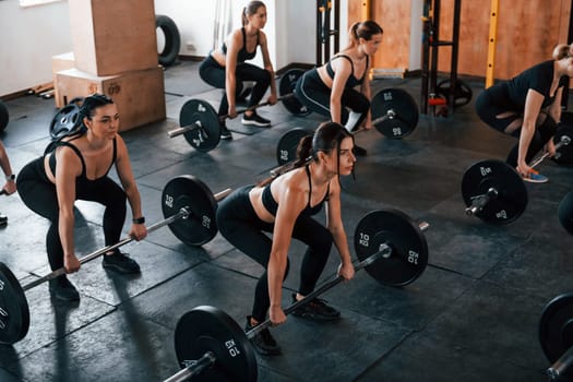 Squats with barbell. Group of young sportive people have crossfit day indoors in gym.