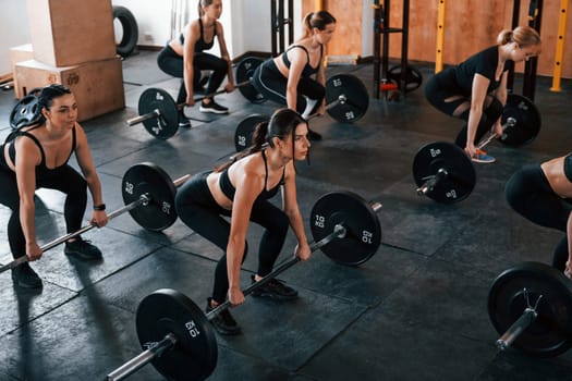 Squats with barbell. Group of young sportive people have crossfit day indoors in gym.