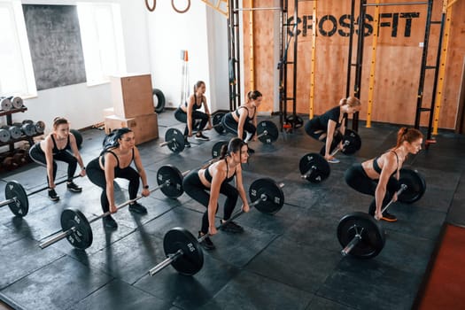 Squats with barbell. Group of young sportive people have crossfit day indoors in gym.