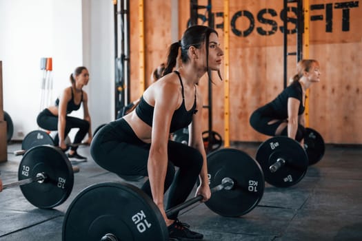 Squats with barbell. Group of young sportive people have crossfit day indoors in gym.