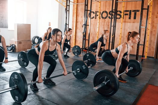 Squats with barbell. Group of young sportive people have crossfit day indoors in gym.