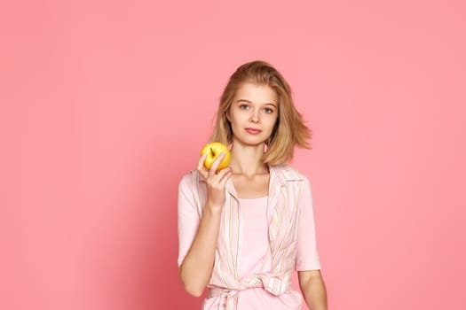 blonde woman holding fresh apple on pink background.