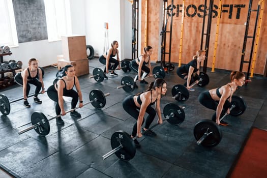 Squats with barbell. Group of young sportive people have crossfit day indoors in gym.