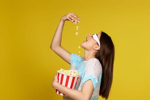 beautiful caucasian woman in 3d glasses eating popcorn on yellow background.