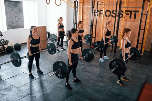 Squats with barbell. Group of young sportive people have crossfit day indoors in gym.