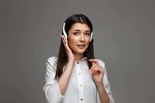 pretty helpline operator woman with headphones and microphone on gray background. girl surprised by what she heard