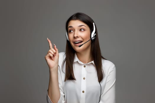 beautiful woman with headset holding index finger up with new idea on gray studio background. Call center, business people concept