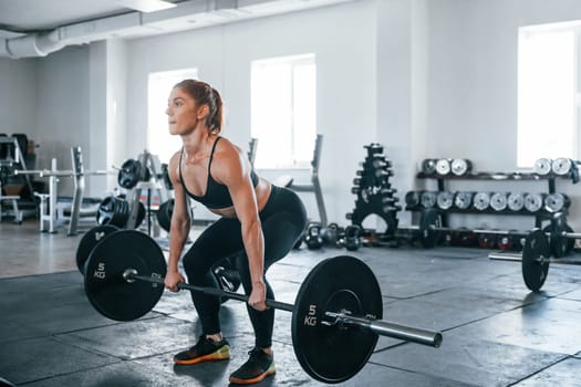Young fitness woman with slim type of body doing exercises by using barbell.
