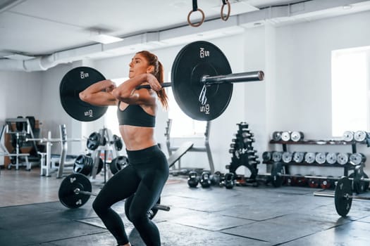 Young fitness woman with slim type of body doing exercises by using barbell.