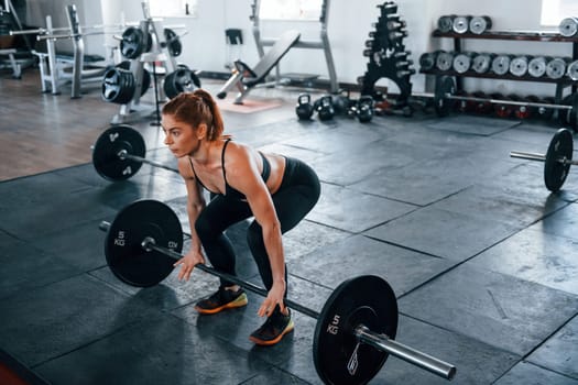 Young fitness woman with slim type of body doing exercises by using barbell.