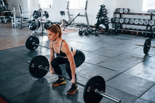 Young fitness woman with slim type of body doing exercises by using barbell.