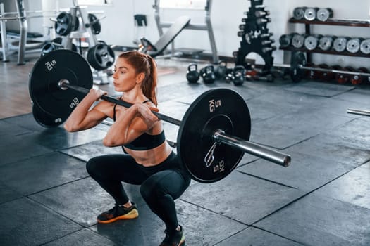 Young fitness woman with slim type of body doing exercises by using barbell.