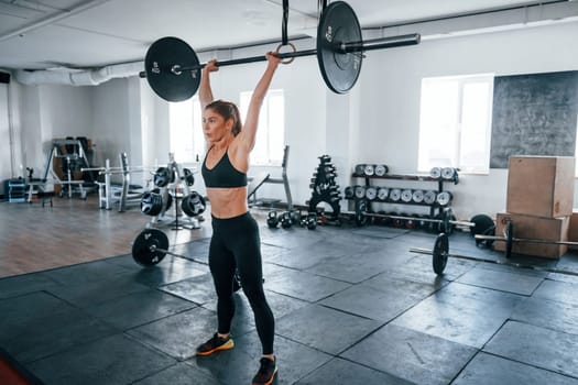 Young fitness woman with slim type of body doing exercises by using barbell.