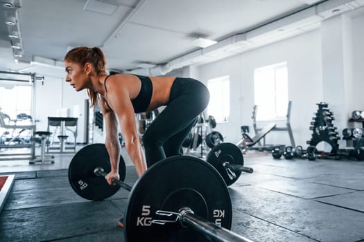 Young fitness woman with slim type of body doing exercises by using barbell.