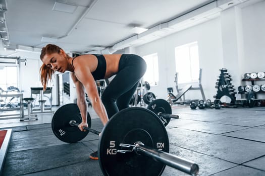 Young fitness woman with slim type of body doing exercises by using barbell.