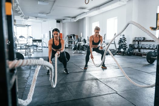 Young people with sportive body shapes doing crossfit by using knots.