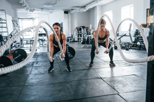 Young people with sportive body shapes doing crossfit by using knots.