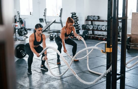 Young people with sportive body shapes doing crossfit by using knots.