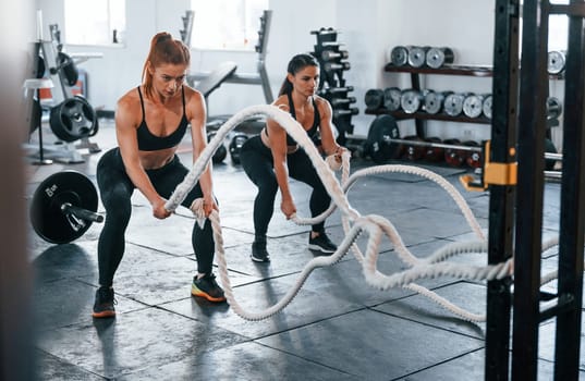 Young people with sportive body shapes doing crossfit by using knots.