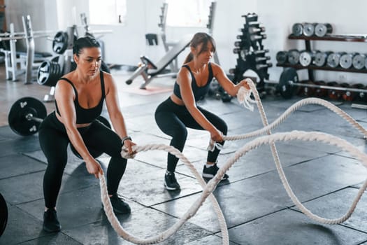 Young people with sportive body shapes doing crossfit by using knots.