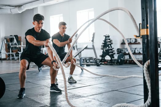 Young people with sportive body shapes doing crossfit by using knots.