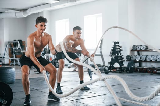 Young people with sportive body shapes doing crossfit by using knots.