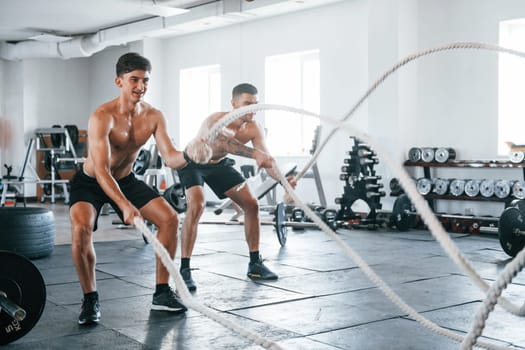 Young people with sportive body shapes doing crossfit by using knots.