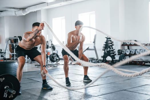 Young people with sportive body shapes doing crossfit by using knots.