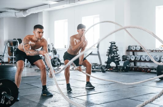 Young people with sportive body shapes doing crossfit by using knots.
