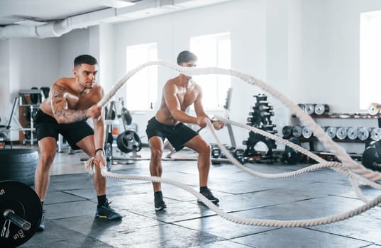 Young people with sportive body shapes doing crossfit by using knots.