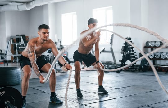 Young people with sportive body shapes doing crossfit by using knots.