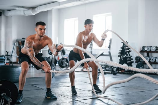 Young people with sportive body shapes doing crossfit by using knots.