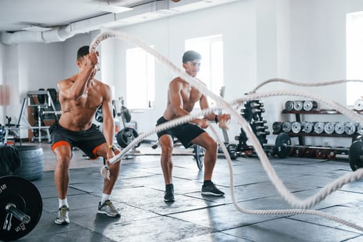 Young people with sportive body shapes doing crossfit by using knots.
