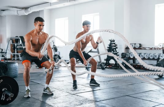 Young people with sportive body shapes doing crossfit by using knots.