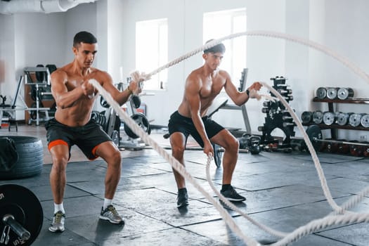 Young people with sportive body shapes doing crossfit by using knots.
