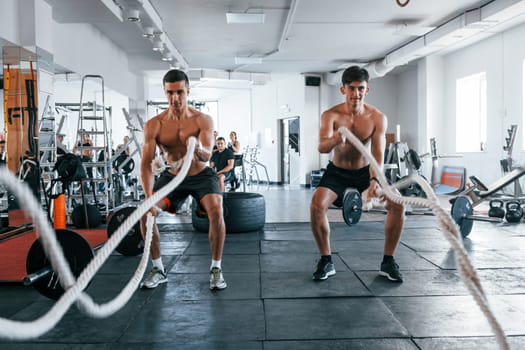 Young people with sportive body shapes doing crossfit by using knots.