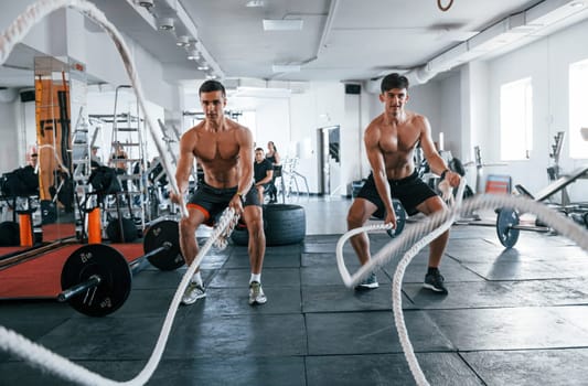 Young people with sportive body shapes doing crossfit by using knots.