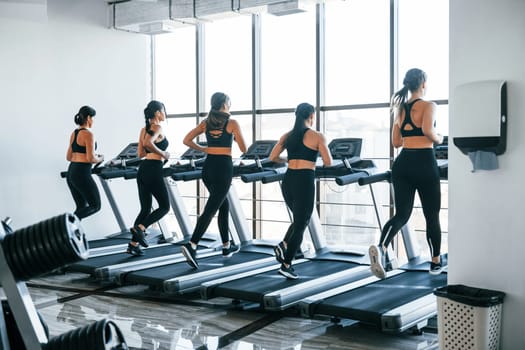 Running on a treadmill. Group of young sportive people have crossfit day indoors in gym.
