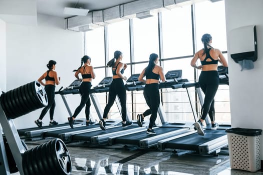 Running on a treadmill. Group of young sportive people have crossfit day indoors in gym.