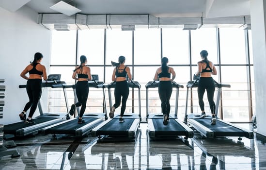 Running on a treadmill. Group of young sportive people have crossfit day indoors in gym.