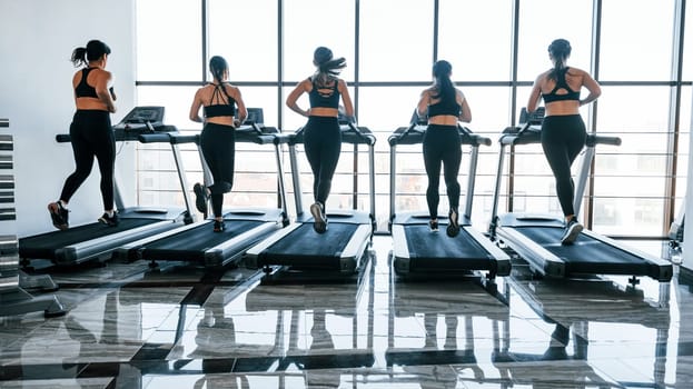 Running on a treadmill. Group of young sportive people have crossfit day indoors in gym.
