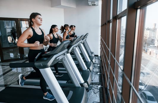 Running on a treadmill. Group of young sportive people have crossfit day indoors in gym.