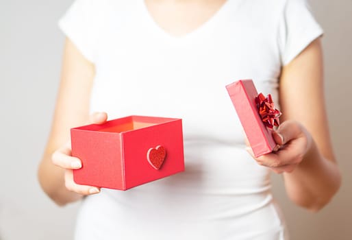 Valentine gift. Close up shot of the female hands opening a small gift in a red box with a heart.