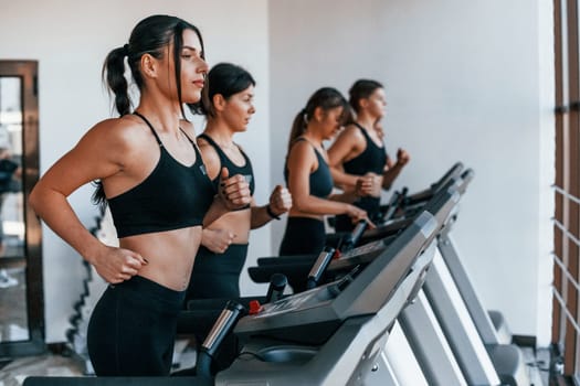 Running on a treadmill. Group of young sportive people have crossfit day indoors in gym.