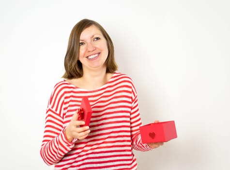 Portrait of a happy smiling pretty girl in red and white shirt opening a red present box on the white background. Valentines day concept.