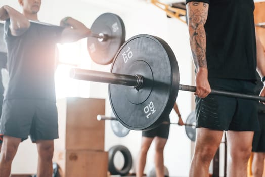 Lifting barbell. Group of young sportive people have crossfit day indoors in gym.