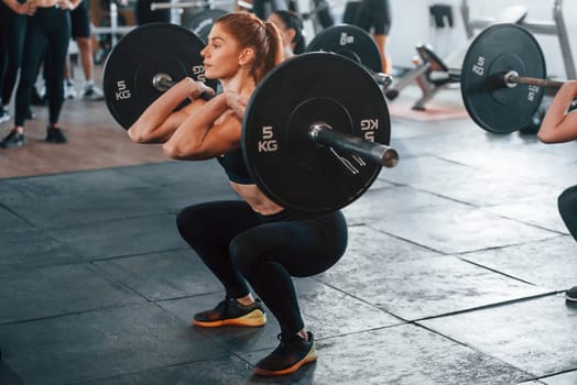 Lifting barbell. Group of young sportive people have crossfit day indoors in gym.