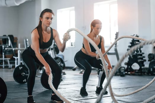 Busy by doing exercises. Group of young sportive people have crossfit day indoors in gym.